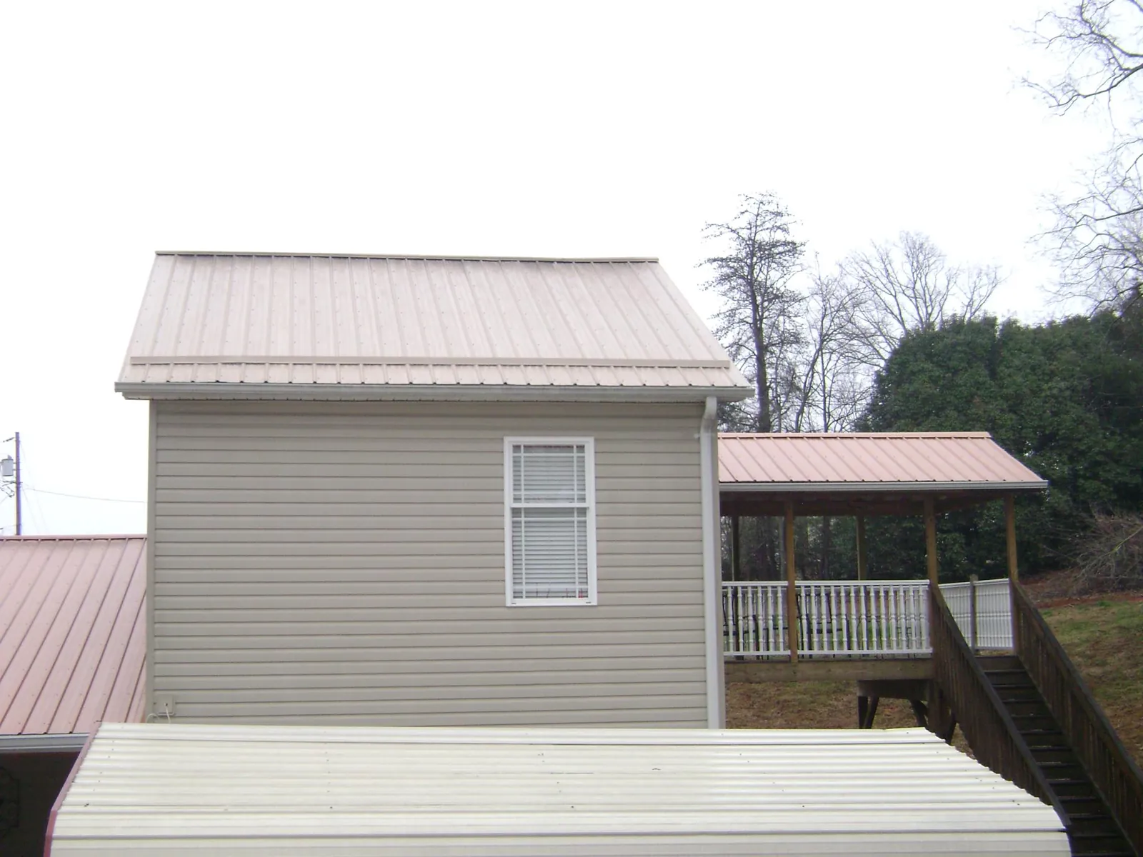 Tan metal roofs on a two story addition and attached porch, from a Roof Replacement job in Springfield